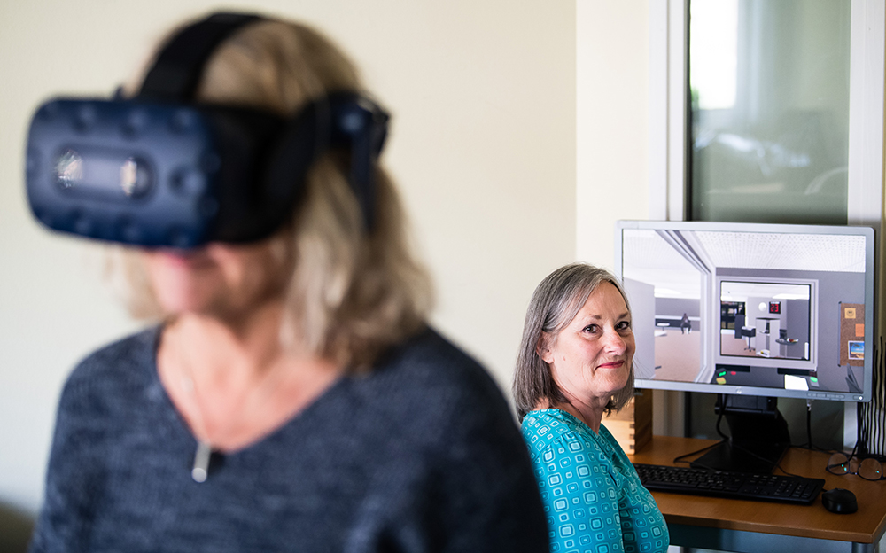Ingrid Irekvist och Ann-Britt Uddgren är enhetschefer på SAF i Mölndal och engagerade i VR-projektet. Ingrid bär utrustningen som den som VR-tränar har på sig och på skärmen syns den virtuella receptionsmiljön. Foto: Mathias Bergeld / BILDBYRÅN